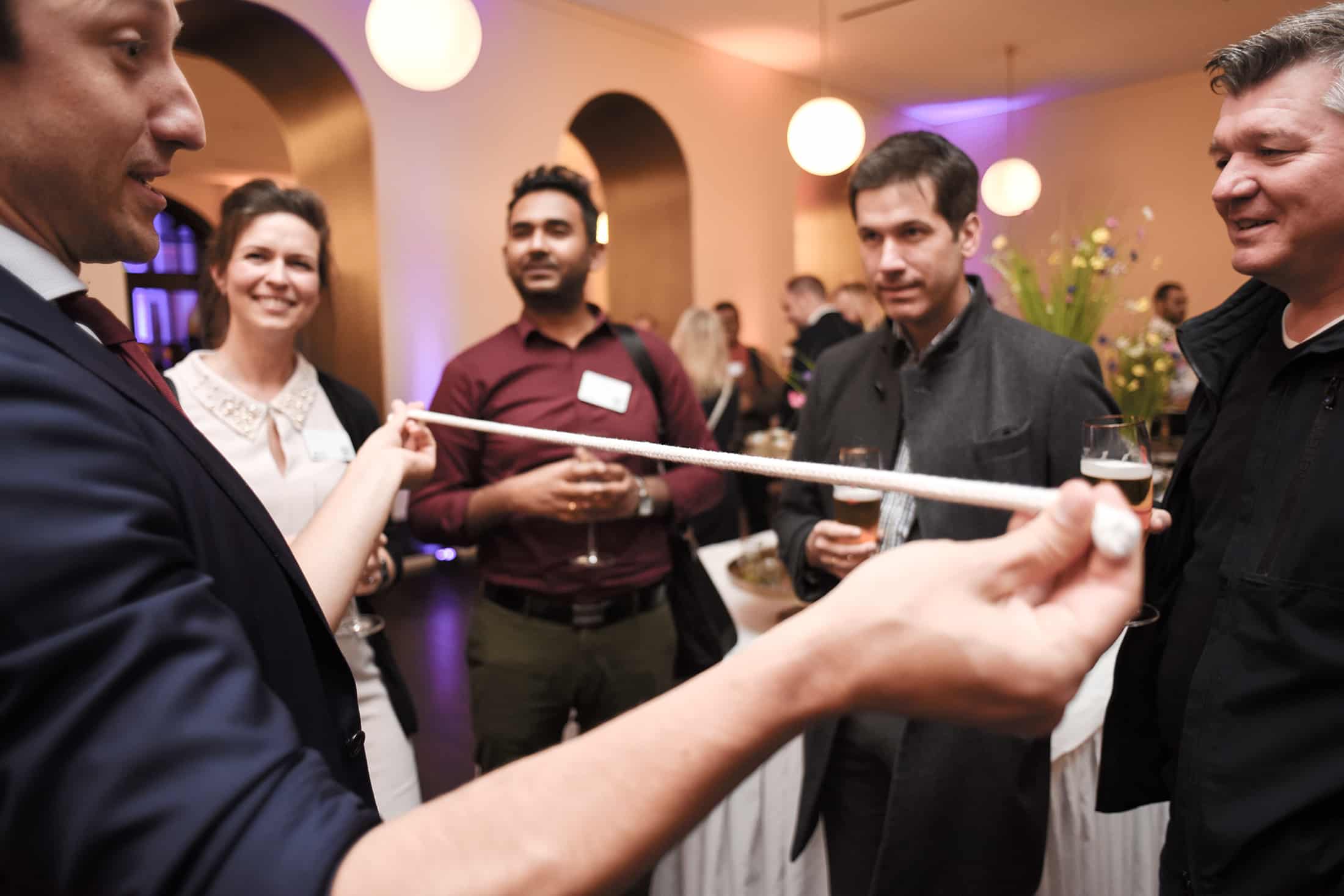 The event magician Fabian Schneekind is presenting a magic trick with a pieve of rope to the international guests of a business event.