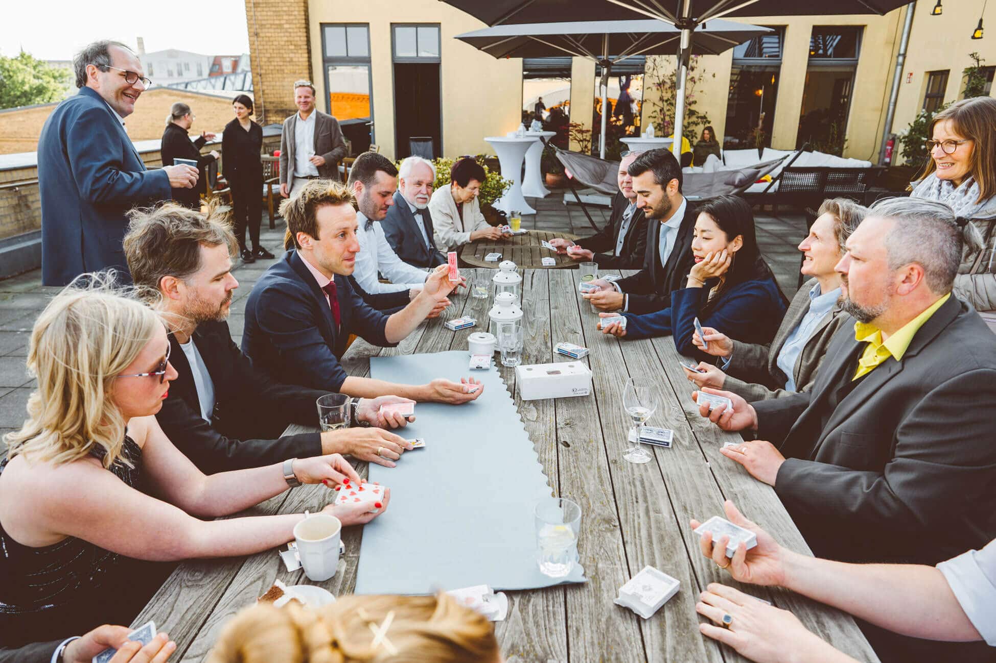 At a team-building event, the participants listen attentively as the magician Fabian Schneekind conducts his magic workshop. They are enjoying it.